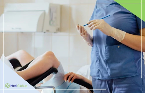 PAP-test для диагностики рака шейки матки Гинеколог в синей медицинской форме и перчатках готовит инструмент для взятия мазка; пациентка лежит на гинекологическом кресле