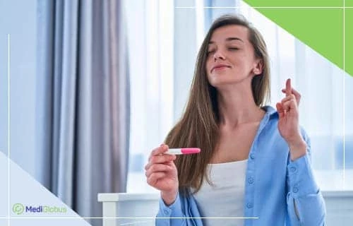 Які шанси завагітніти після ЕКЗ? Жінка в блакитній сорочці тримає тест на вагітність і схрещує пальці