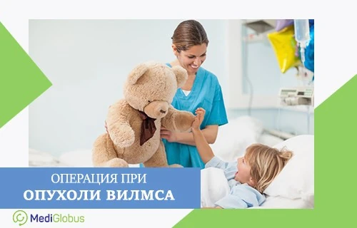 Операция при опухоли Вилмса Женщина в медицинской форме держит игрушечного медведя и показывает его лежащему в больничной кровати ребенку