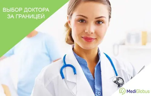 Правила выбора доктора за границей Молодая женщина‑врач в белом халате со стетоскопом на шее, улыбается, на заднем плане виден коллега в медицинской форме
