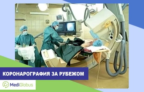 Стоимость коронарографии за рубежом Пациент лежит на столе в операционной, рядом два врача в хирургических халатах и масках проводят коронарографию; над пациентом установлено крупное рентгеновское оборудование, на мониторе виден снимок сосудов сердца.