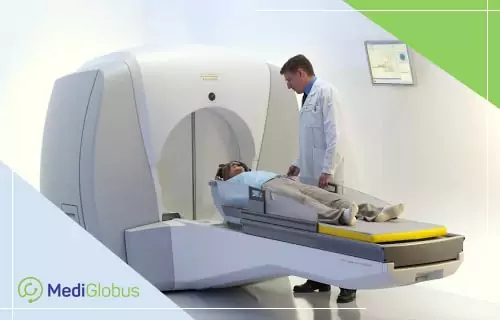 Что такое Гамма‑нож Пациент лежит на столе радиохирургической установки Gamma Knife, рядом стоит врач в белом халате, контролирующий процесс