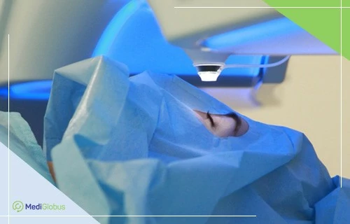 Relexsmile - самый щадящий метод коррекции зрения Лицо человека накрыто стерильной синей тканью, открыт только глаз, на который направлен апарат для лазерной коррекции зрения