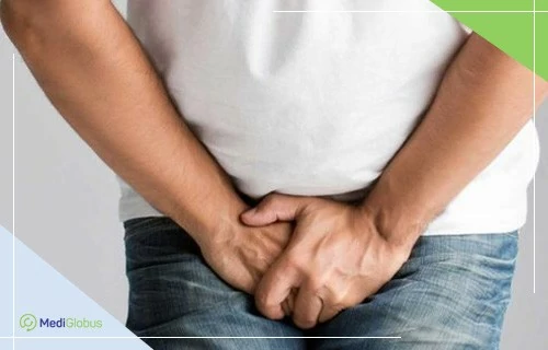 лікування раку яєчок чоловік у білій футболці та джинсах тримається руками за пахову ділянку, відчуваючи дискомфорт або біль