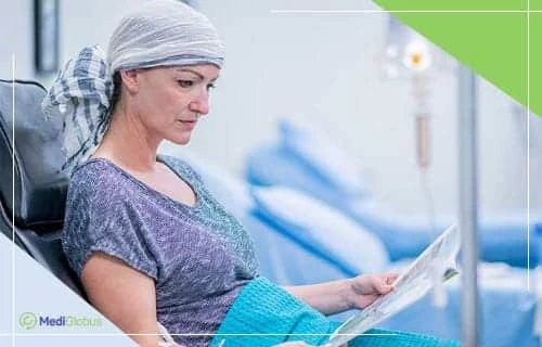 Сучасна хіміотерапія — нові підходи до лікування раку печінки Жінка з покритою головою сидить у кріслі медичного центру, читає журнал; на задньому плані видно кушетки та стійку з крапельницею