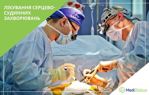 Двоє хірургів у операційній проводять серцево-судинну операцію; обидва в стерильних халатах, масках і захисних окулярах, працюють під яскравим світлом операційних ламп, на тлі видно медичні прилади.