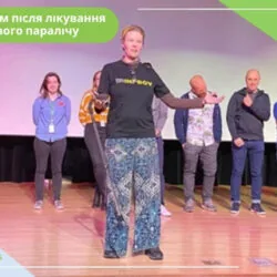 Відгуки про лікування лицьового паралічу Жінка стоїть на сцені і щось розповідає, позаду неї группа людей, які уважно слухають її