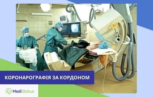 Вартість коронарографії за кордоном Пацієнт лежить на столі в операційній, поруч двоє лікарів у хірургічних халатах і масках проводять коронарографію; над пацієнтом встановлено велике рентгенівське обладнання, на моніторі видно знімок судин серця.