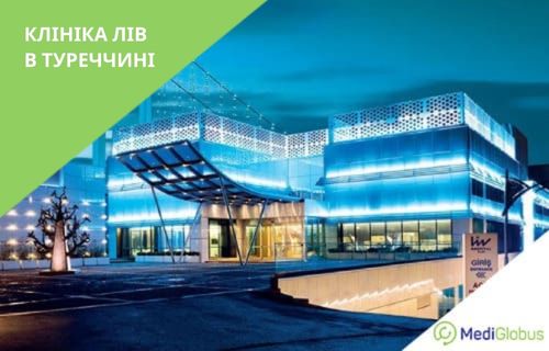 Нейрохірургія в клініці Лів в Туреччині Сучасна будівля клініки зі скляно-металевим фасадом, що ввечері підсвічується блакитним світлом; біля входу — навіс із металевими опорами, поруч — парковка.