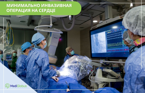 Бригада хирургов проводит малоинвазивную операцию на сердце под контролем визуализации. На большом мониторе в операционной отображаются видео и показатели жизнедеятельности и графики сердцебиения пациента в реальном времени.
